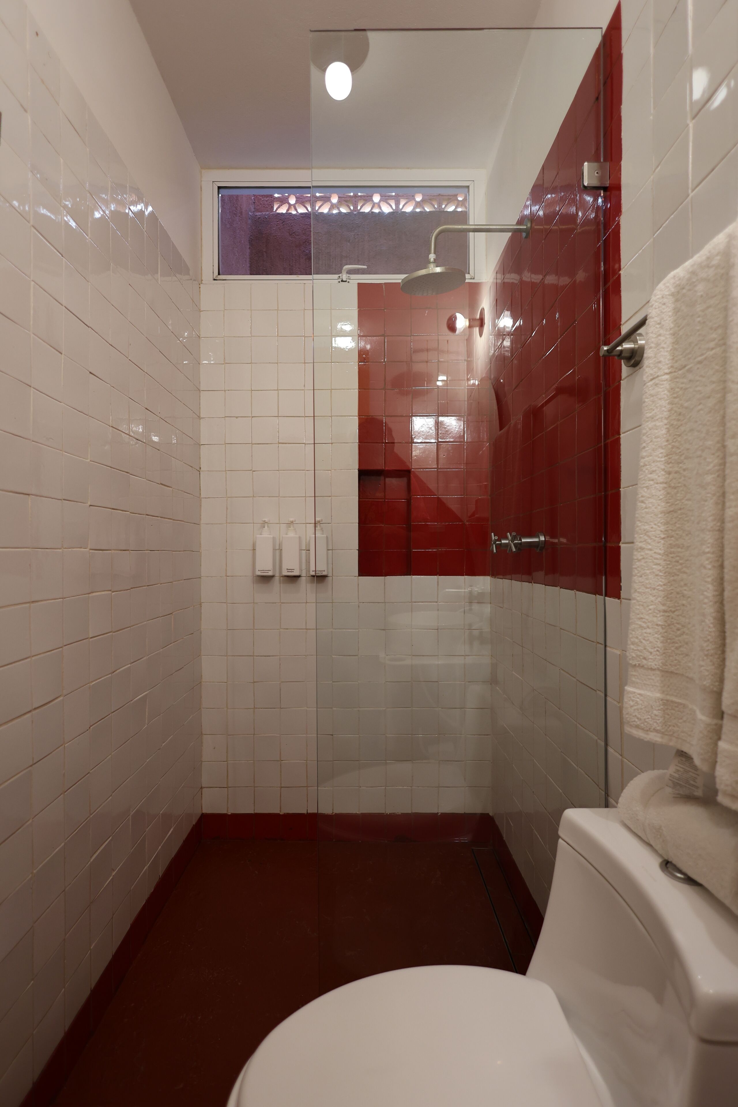 A modern bathroom with white and red tiles, a glass shower enclosure, and a white toilet.