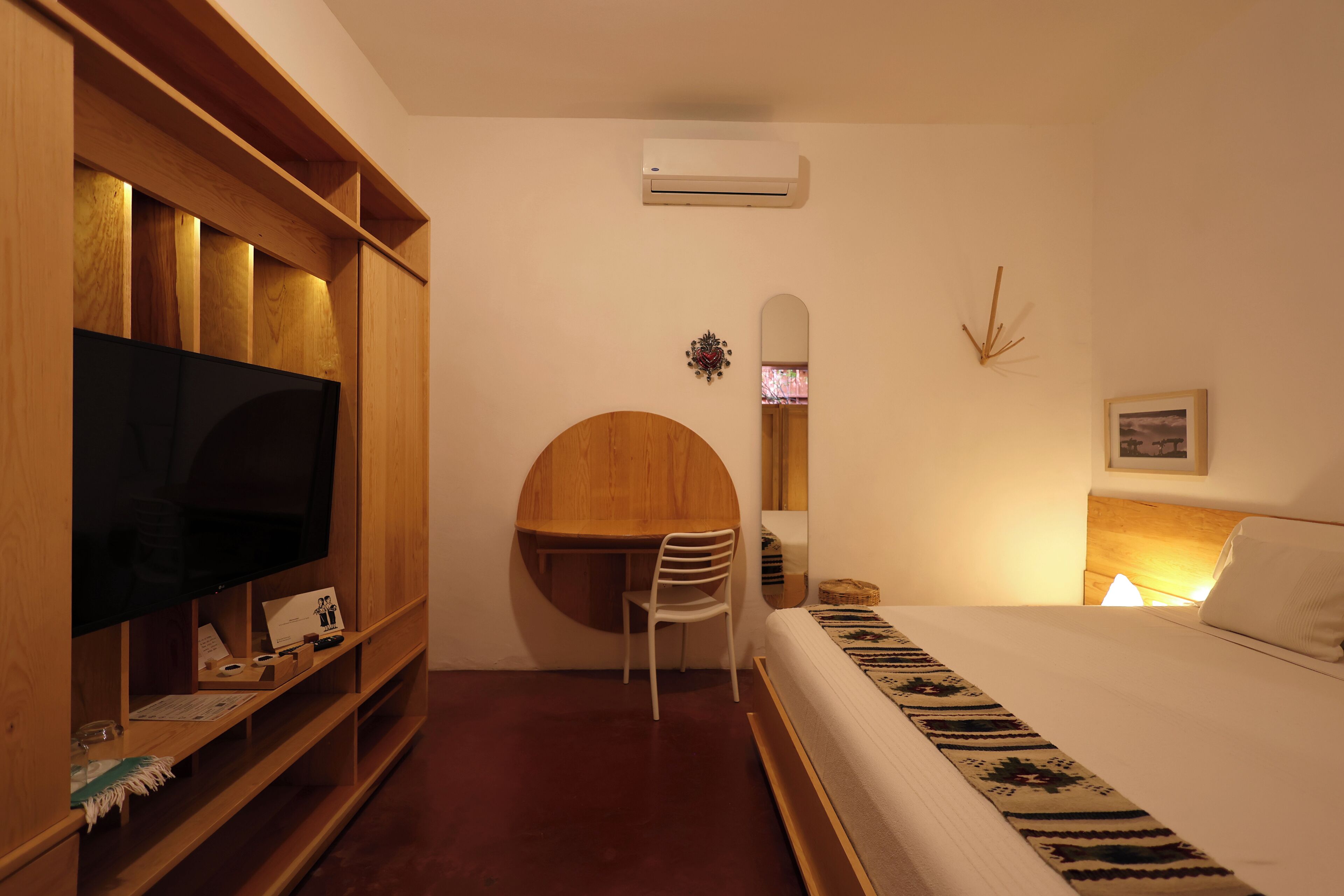 Un dormitorio con cama, escritorio, silla, televisor y espejo.