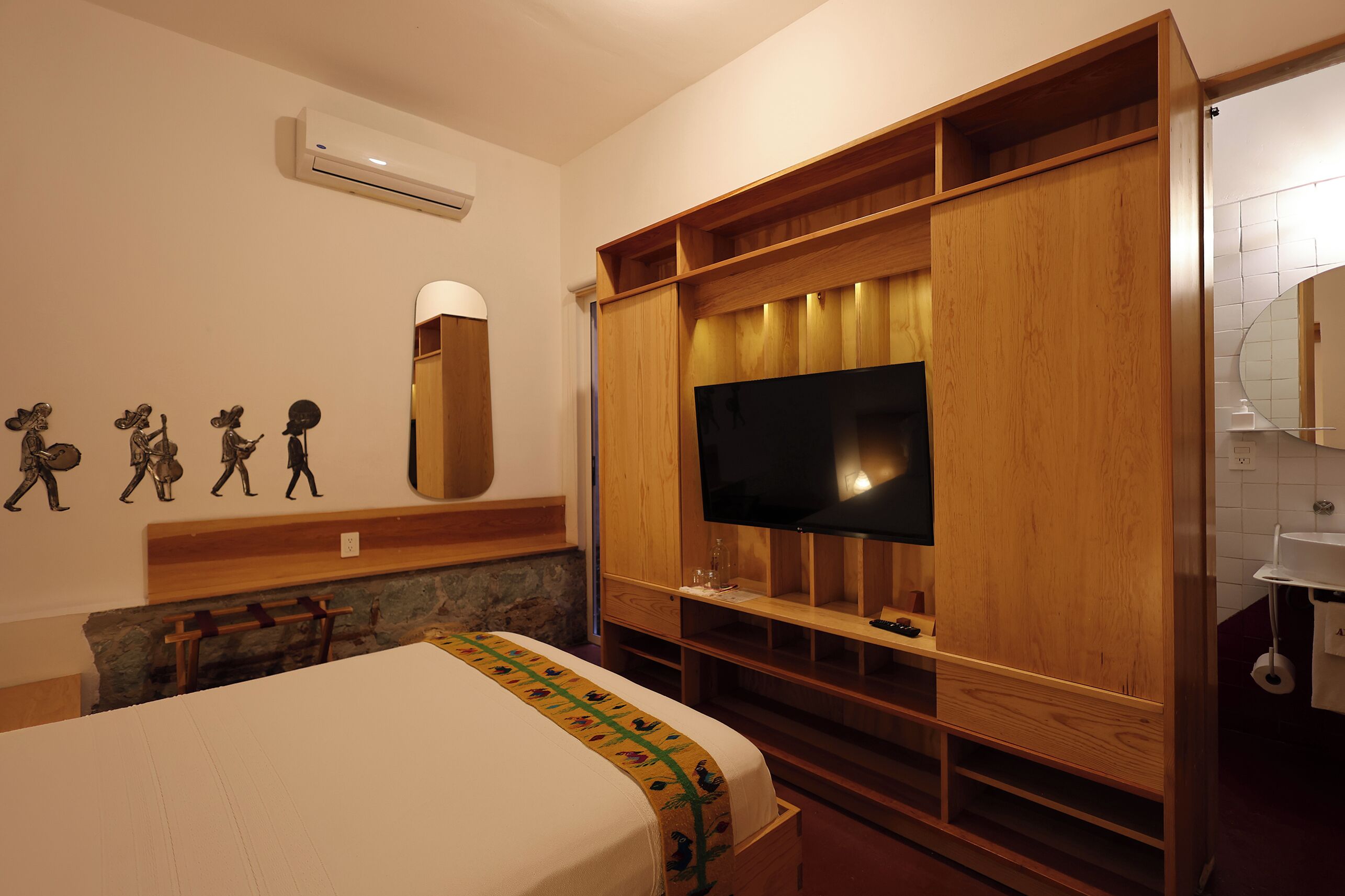 Camera d'albergo con un letto, una TV montata su un mobile in legno, una parete in pietra e un bagno con lavandino e specchio.