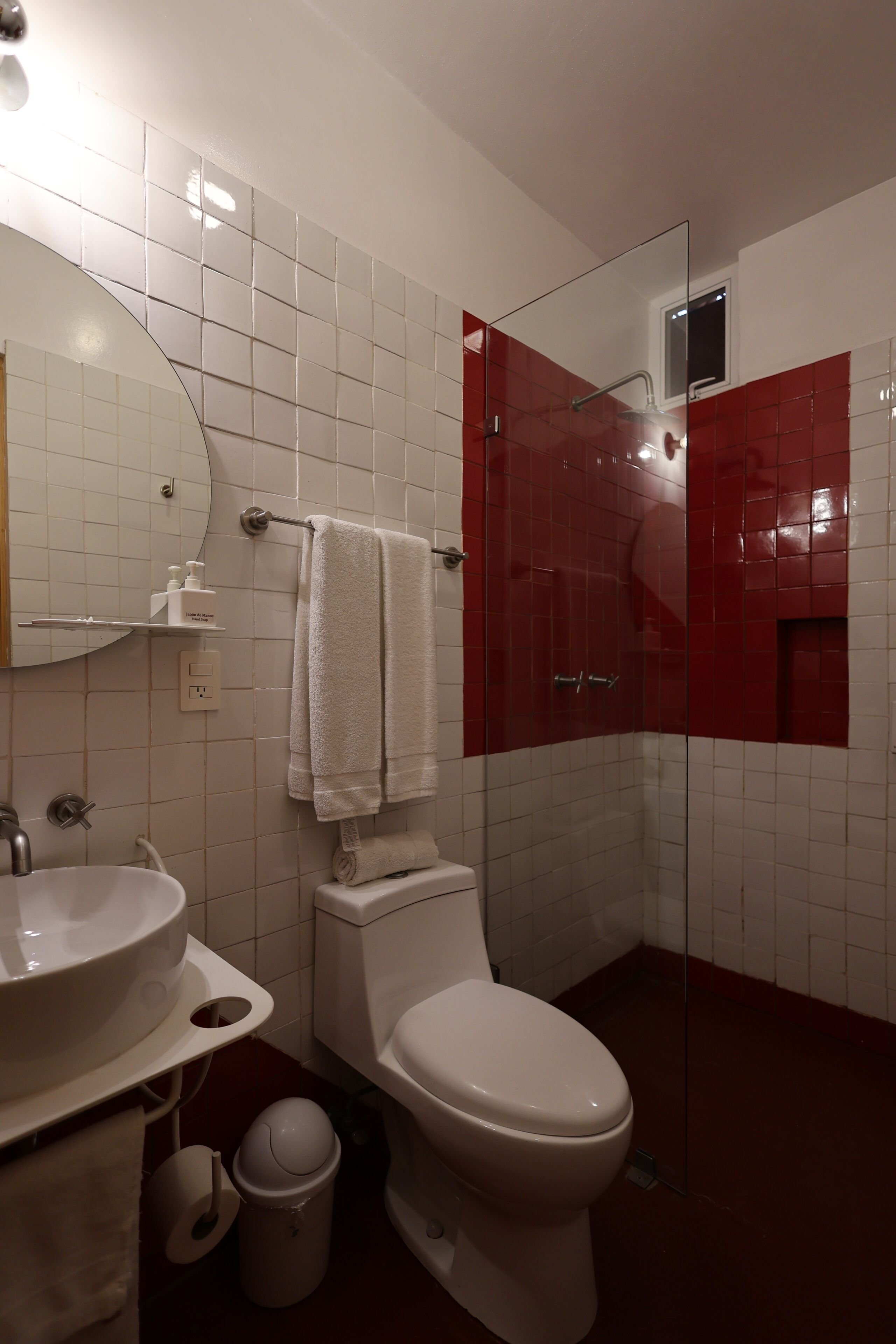 Une salle de bain avec un lavabo blanc, des toilettes, une douche en verre et un mur recouvert de carreaux rouges.