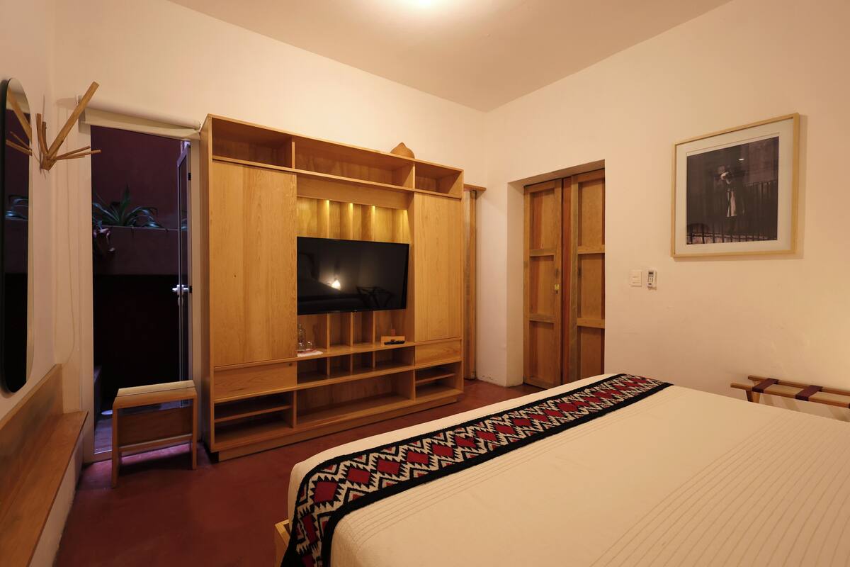 A bedroom with a large bed, a TV on a wooden cabinet, and a wardrobe.