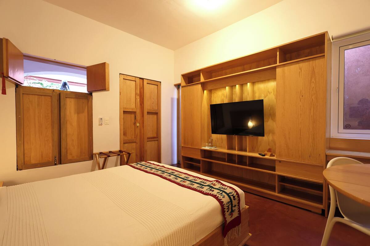 A bedroom with a bed, wooden wardrobe, TV, and a window with a view.