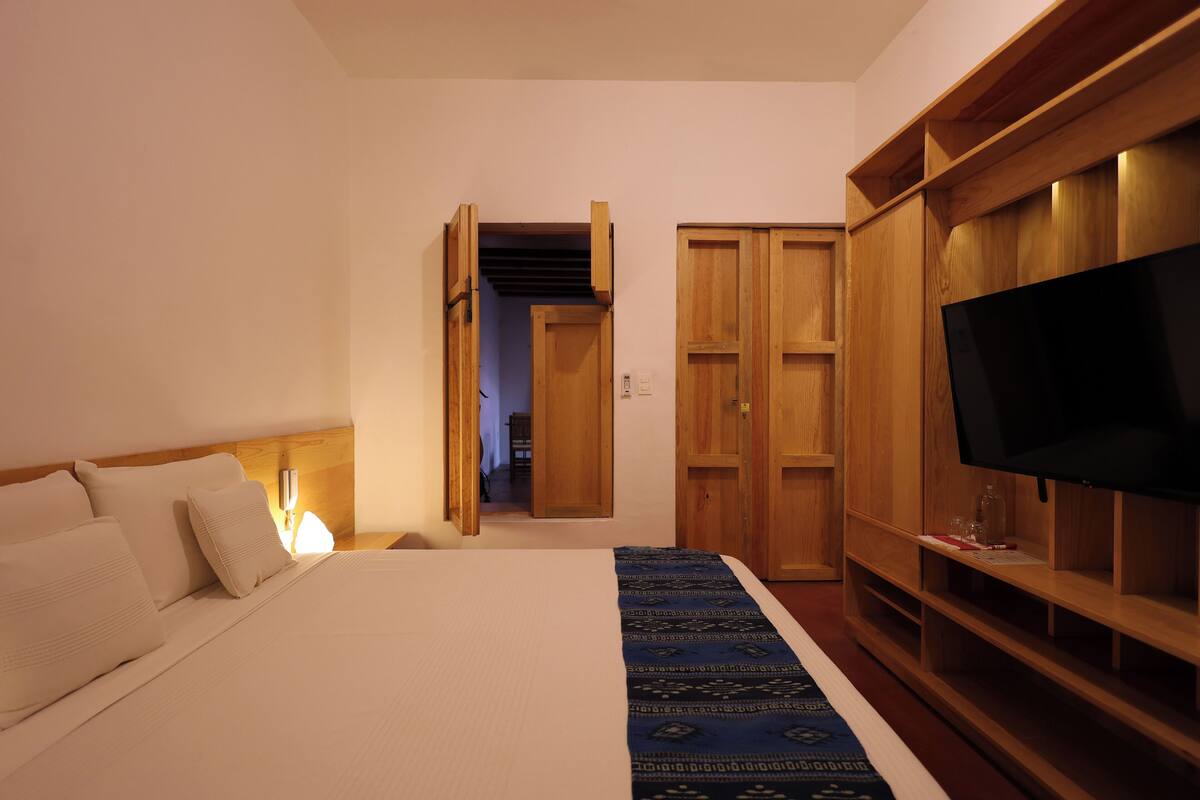 A bedroom with a bed, wooden wardrobe, and a TV.
