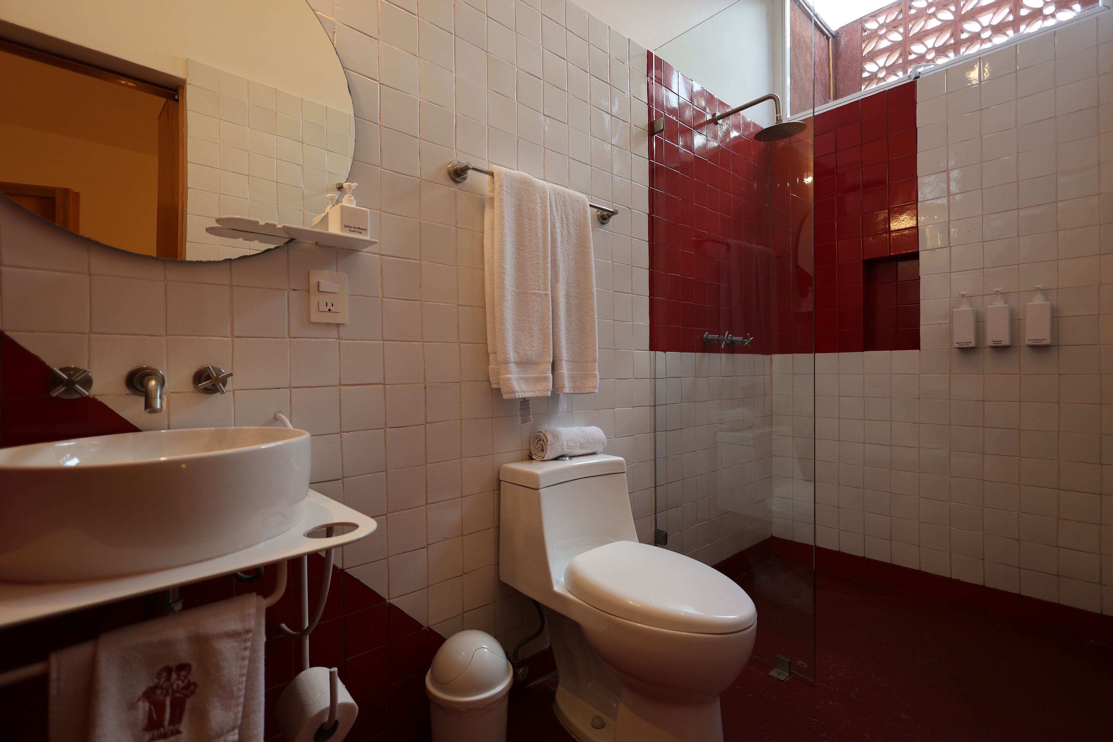 Une salle de bain avec un lavabo blanc, des toilettes et une douche dont le sol est recouvert de carreaux rouges.
