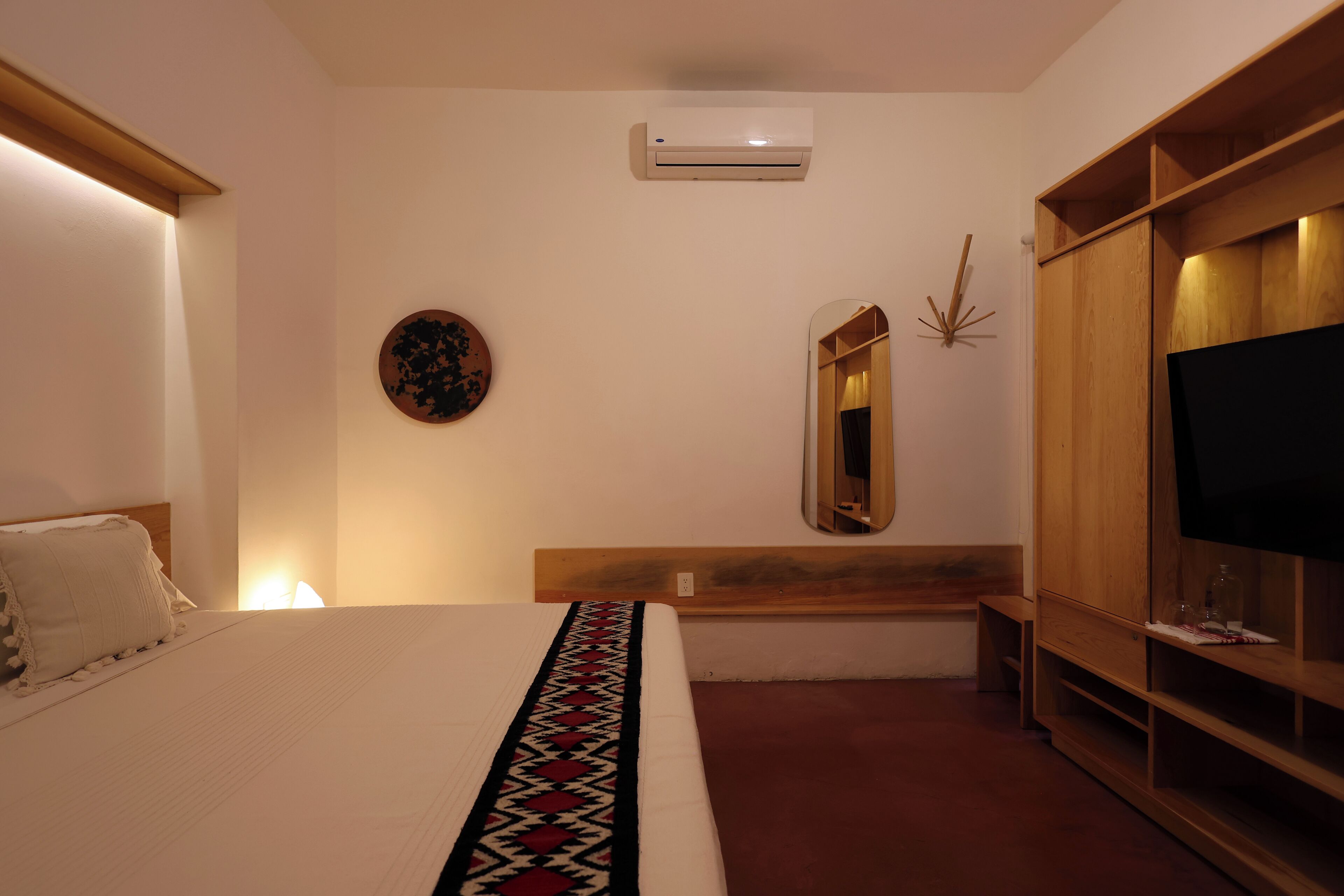 A bedroom with a bed, a TV, a wardrobe, a mirror, and an air conditioner.