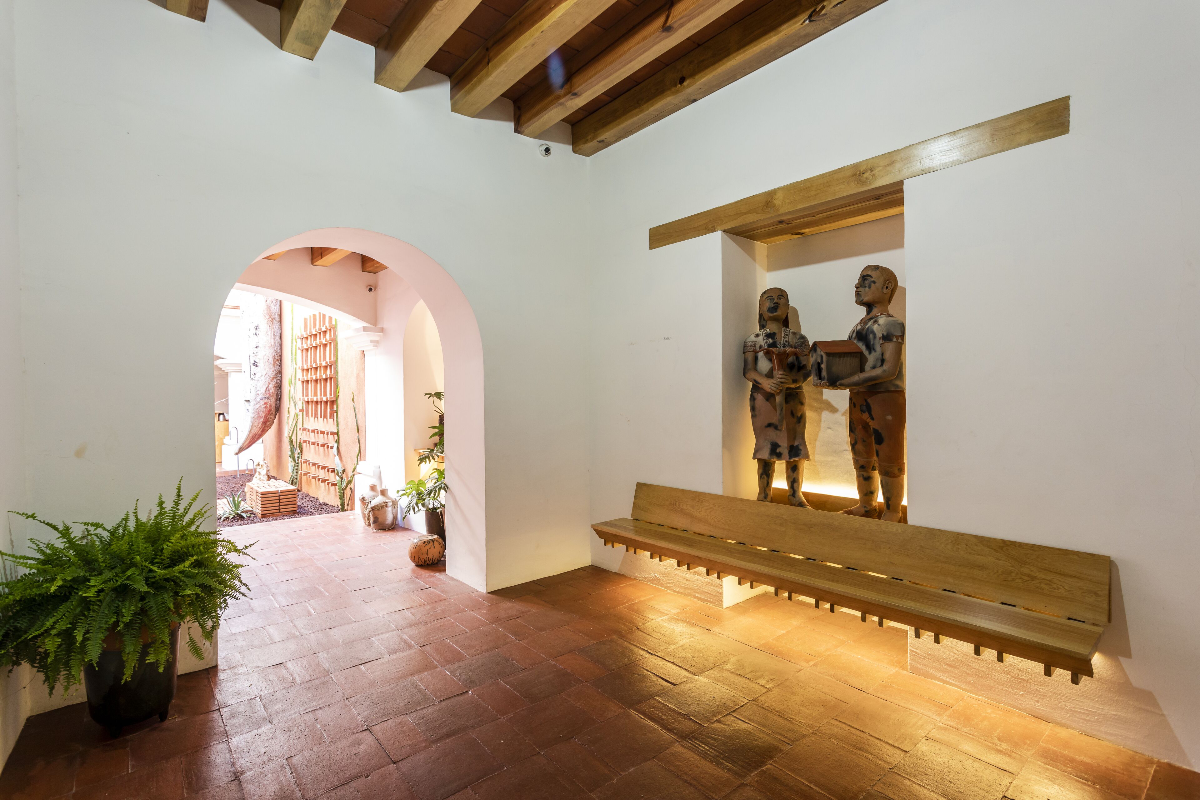 A hallway with a wooden bench, a potted plant, and a wall-mounted sculpture.