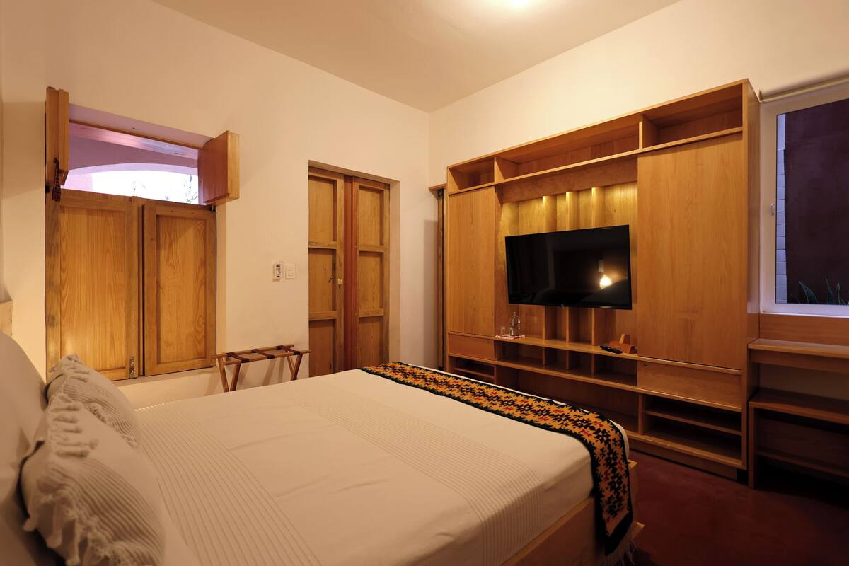 A bedroom with a bed, wooden wardrobe, TV, and built-in shelves.