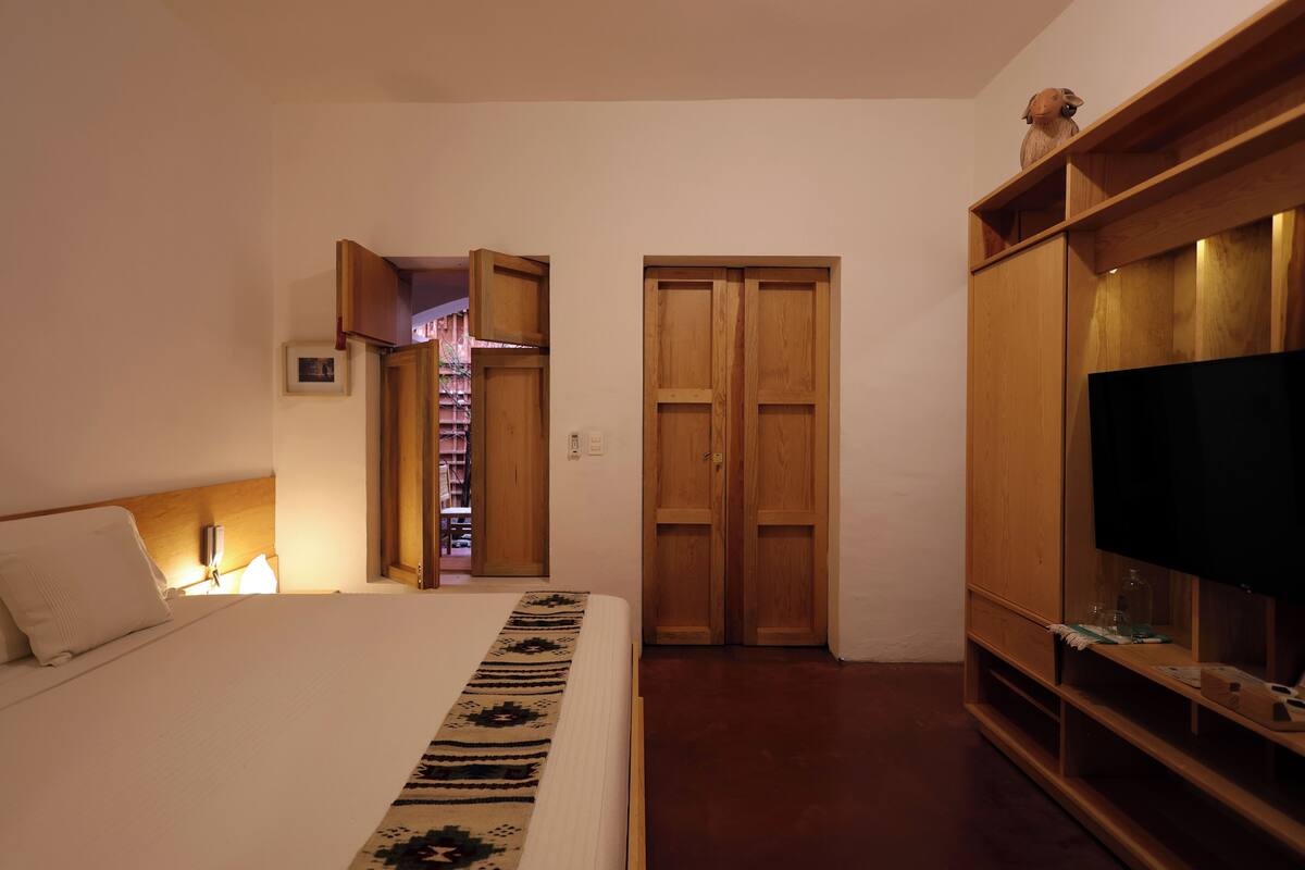 A bedroom with a bed, wooden wardrobe, and a television.