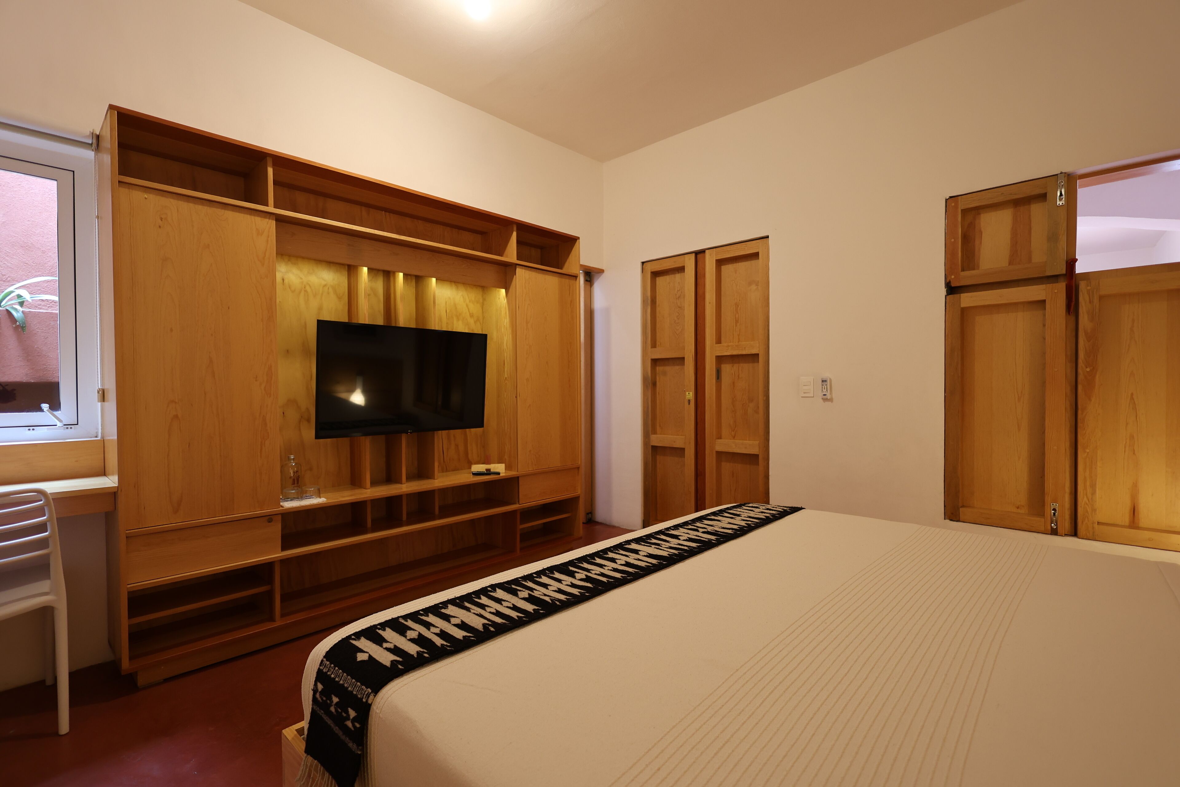 A bedroom with a large bed, wooden wardrobe, built-in TV, and a desk with a chair.