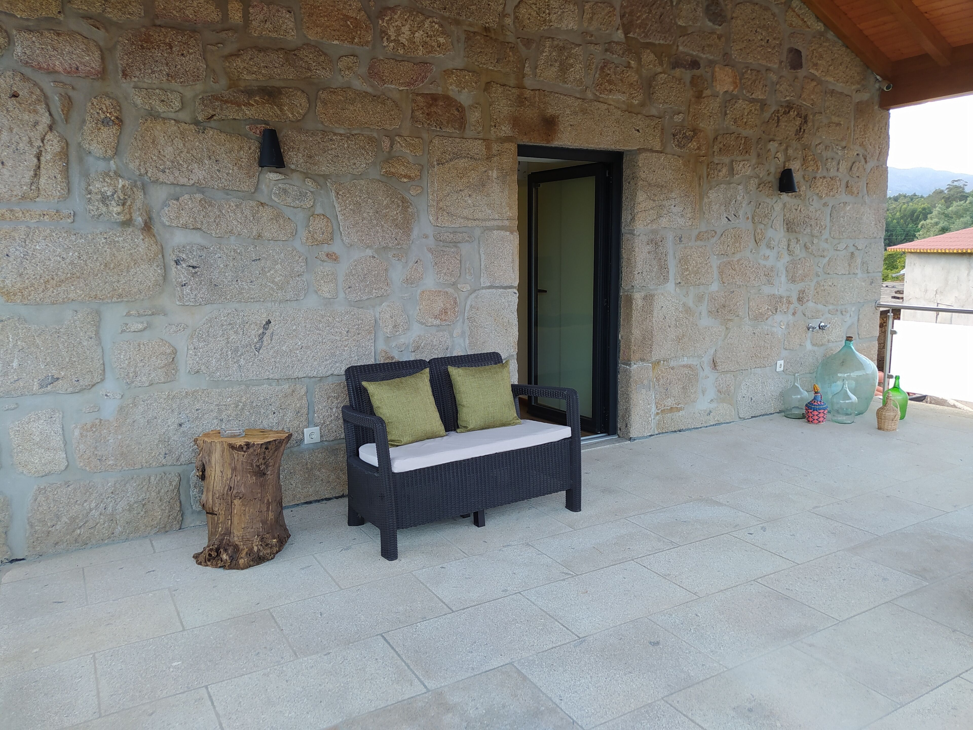 A stone wall with a wicker sofa and a wooden stump.