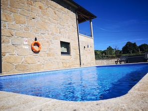 A swimming pool with stone walls, a lifebuoy, and a chair by the pool.