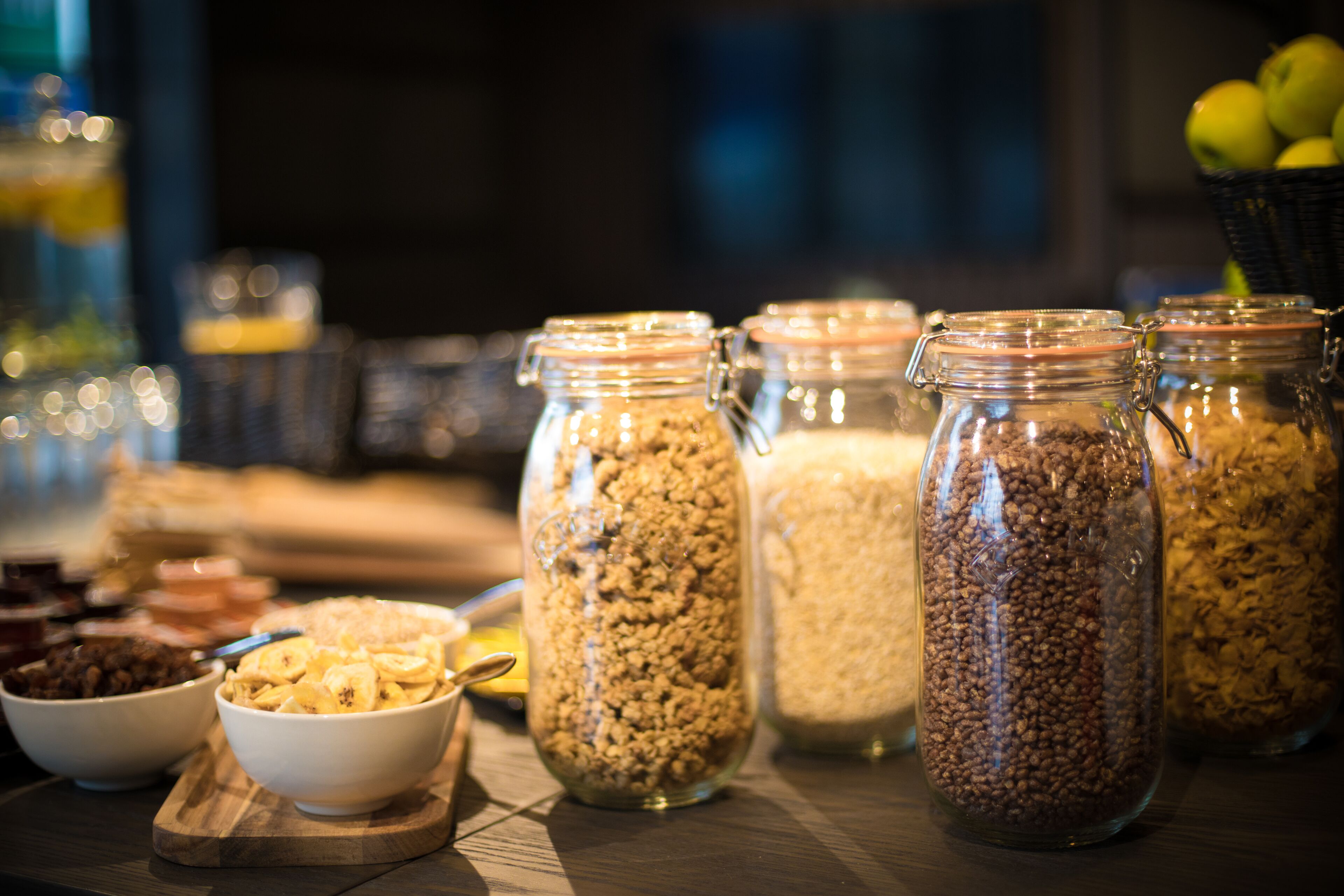 A table with various food items including bowls of cereal and jars of nuts and dried fruits.