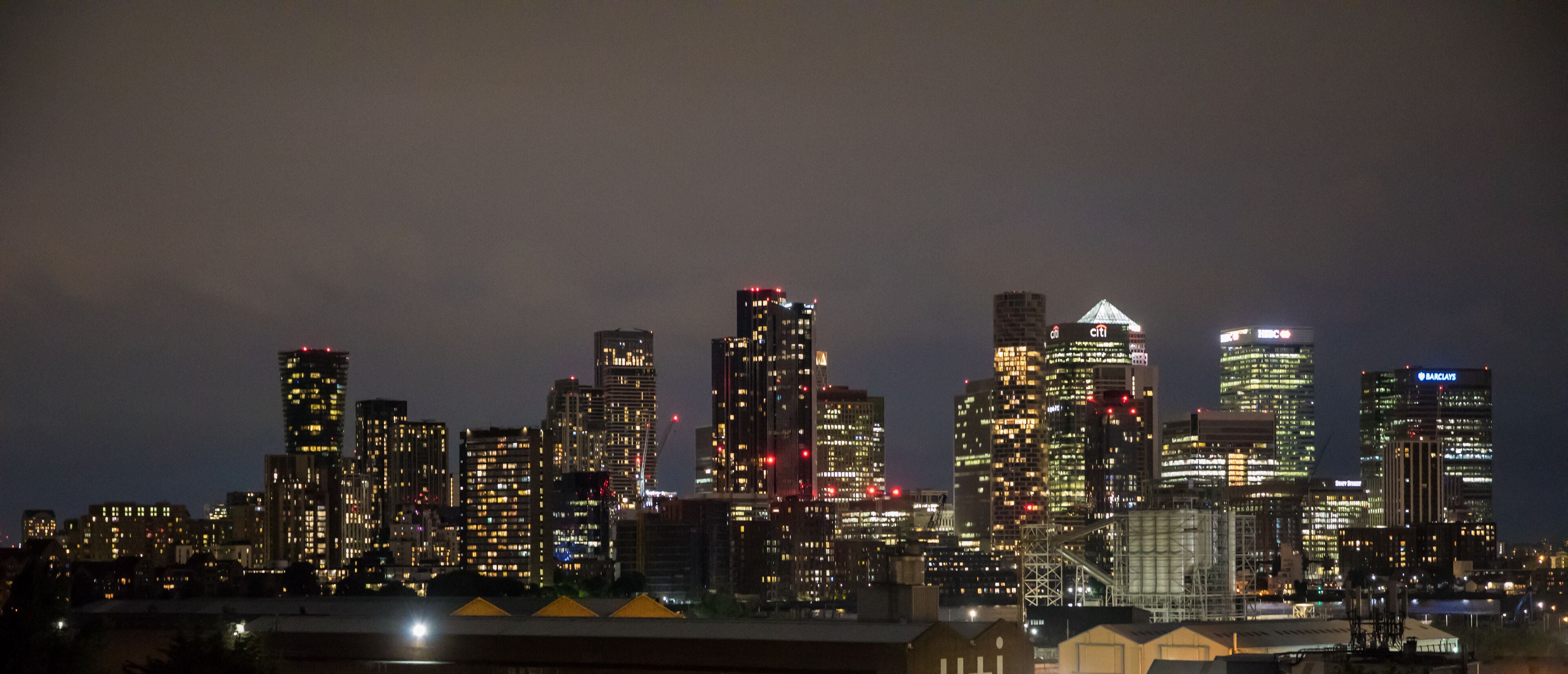 Un horizonte nocturno de la ciudad con edificios iluminados, incluyendo un edificio Barclays destacado.