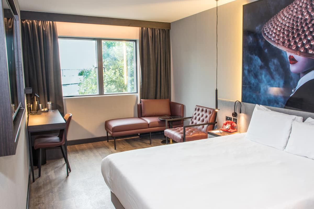 Habitación de hotel con una cama grande, un escritorio con una silla, un sofá y un televisor de gran tamaño montado en la pared.