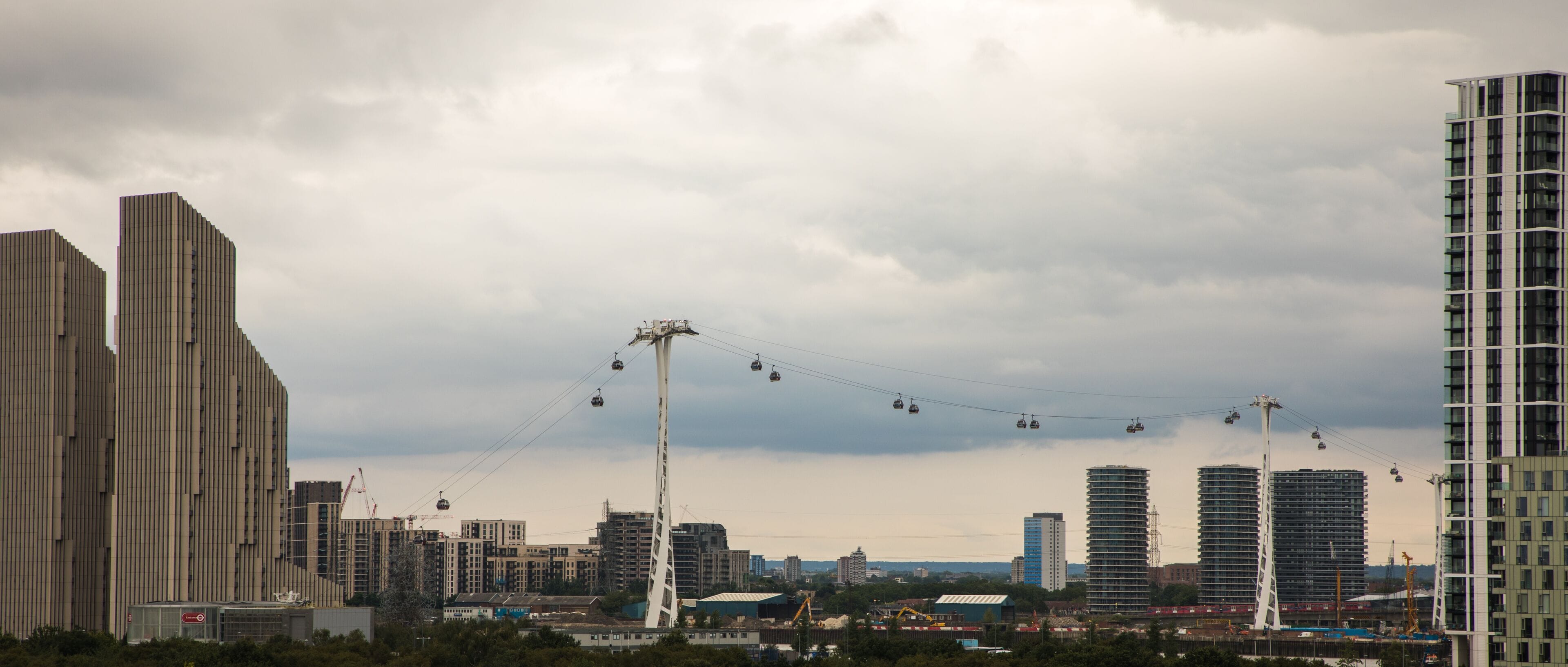 A cityscape with high-rise buildings, a cable car system, and construction cranes.