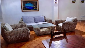 A cozy living area with wicker furniture, a painting of a landscape, and a small table. - Villa Alladin (Sciacca)
