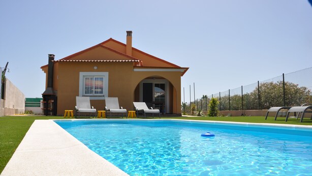 A swimming pool with a house in the background, a clear sky, and a fenced area. - ECO Villa Nazaret with Solar Energy (Antigua)