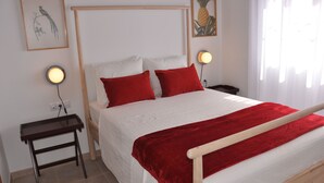 A neatly made bed with a red blanket and pillows, two bedside tables with lamps, and framed artwork on the walls. - ECO Villa Nazaret with Solar Energy (Antigua)