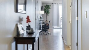 A hallway with a wooden floor, a desk with a plant, and a chair.