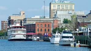 A waterfront with a large white boat docked at a pier, surrounded by buildings and smaller boats.