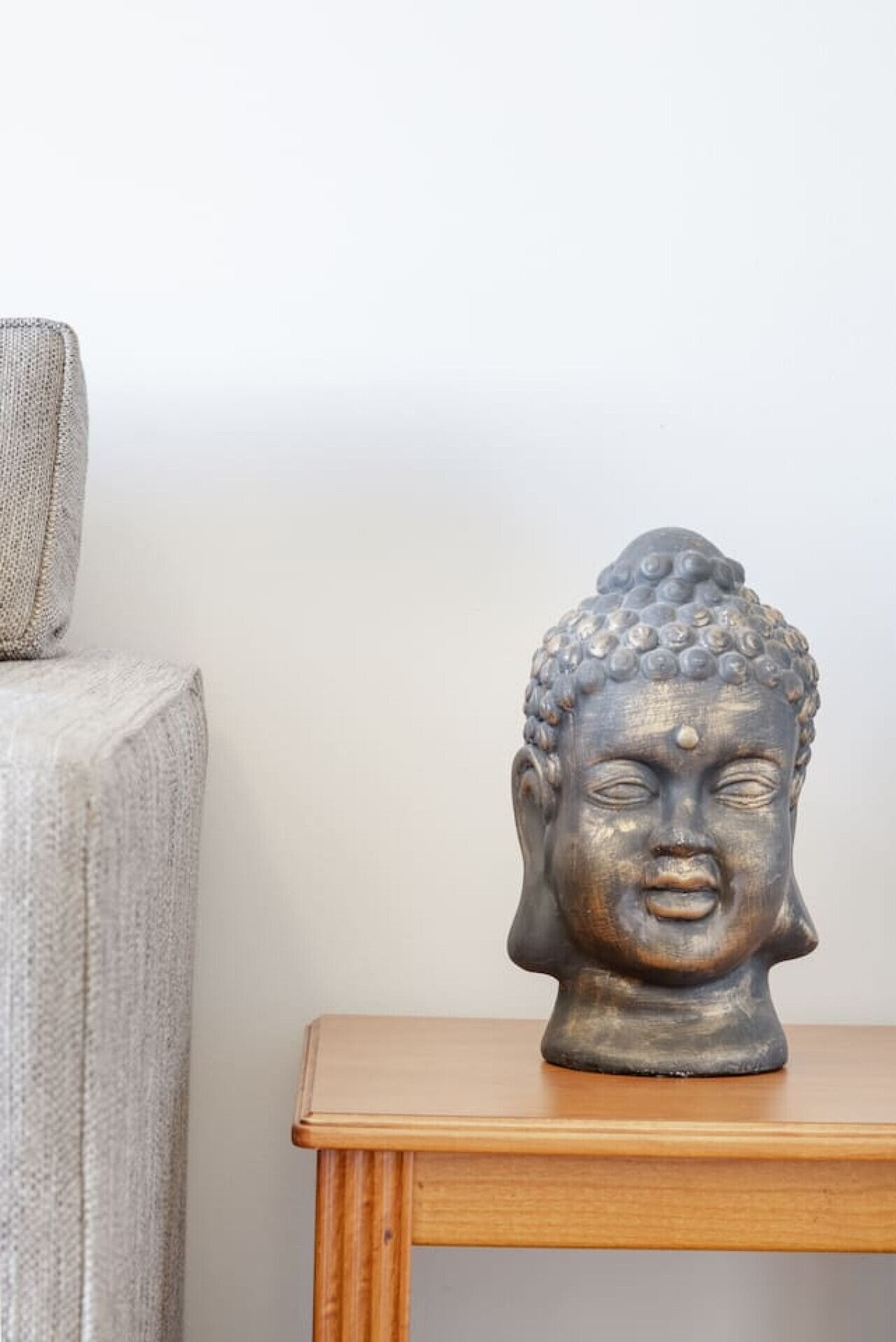 Una escultura de cabeza de Buda sobre una mesa de madera frente a una pared lisa.