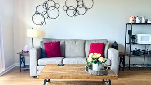 A living room with a grey sofa, red cushions, a wooden coffee table with a basket and flowers, and a wall art piece above.