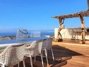Une terrasse avec une table et des chaises, une structure décorative en bois et une vue sur la mer.