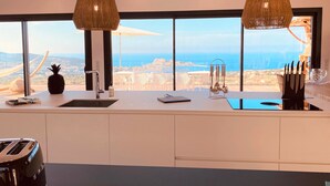 Una cocina moderna con un amplio ventanal que ofrece una vista panorámica, un lavamanos empotrado y dos lámparas colgantes.