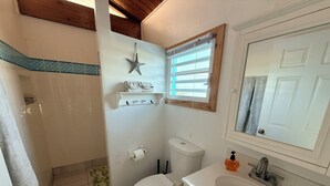 A bathroom with a shower, toilet, sink, and a towel rack with towels. - Beachside Studio with Car (Grand Turk)