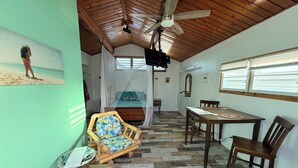 A room with a wooden ceiling, a bed with a canopy, a dining table with chairs, and a chair with a floral cushion. - Beachside Studio with Car (Grand Turk)