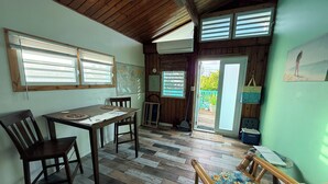 A room with a wooden floor, a dining table with chairs, a sofa, and a large window with blinds. - Beachside Studio with Car (Grand Turk)