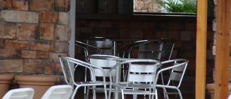 A patio area with a thatched roof, stone wall, metal chairs, and a potted plant.