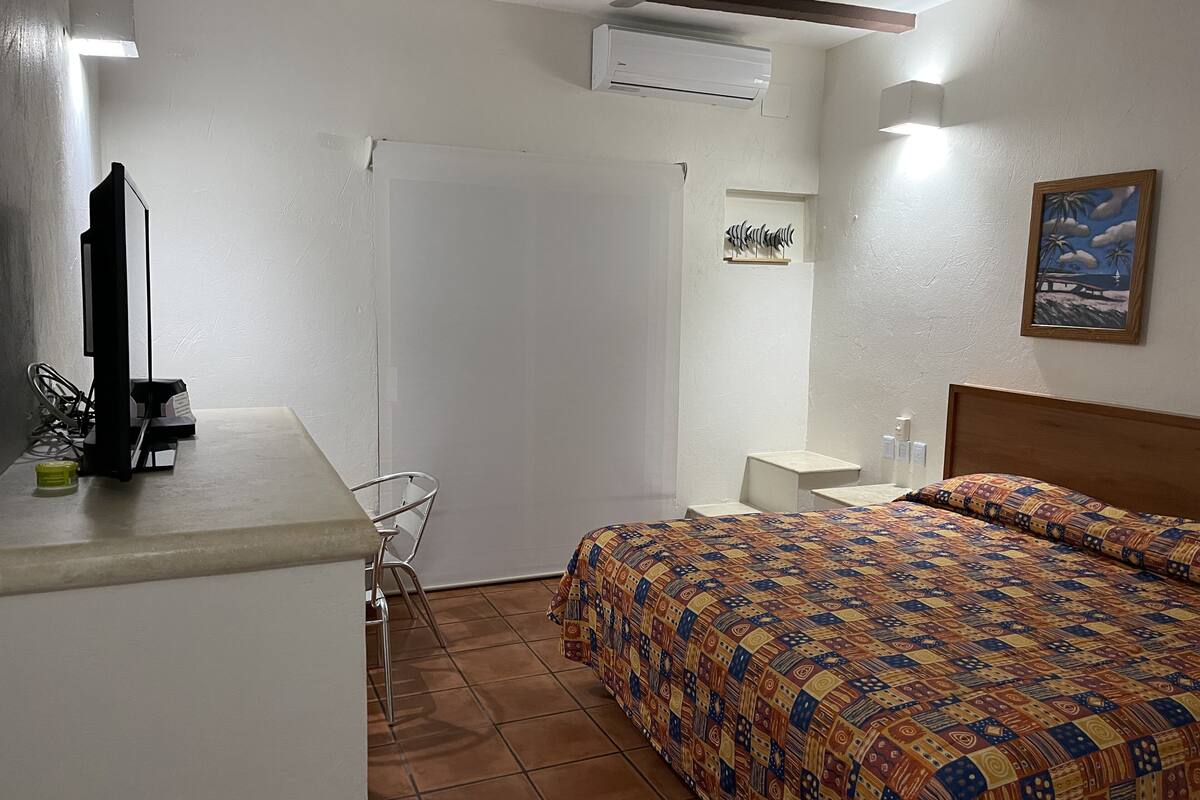 A bedroom with a bed, a desk with a chair, a TV, and an air conditioner.