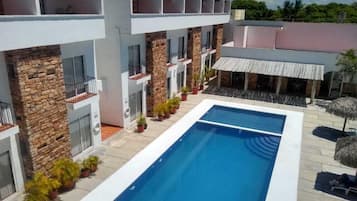 Un edificio moderno con piscina, pilares de piedra y una estructura con techo de paja.