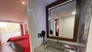 A hotel room with a granite countertop, a large mirror with LED lights, a hairdryer, and a bed with red bedding. - La Mansión del Faro (Tecolutla)