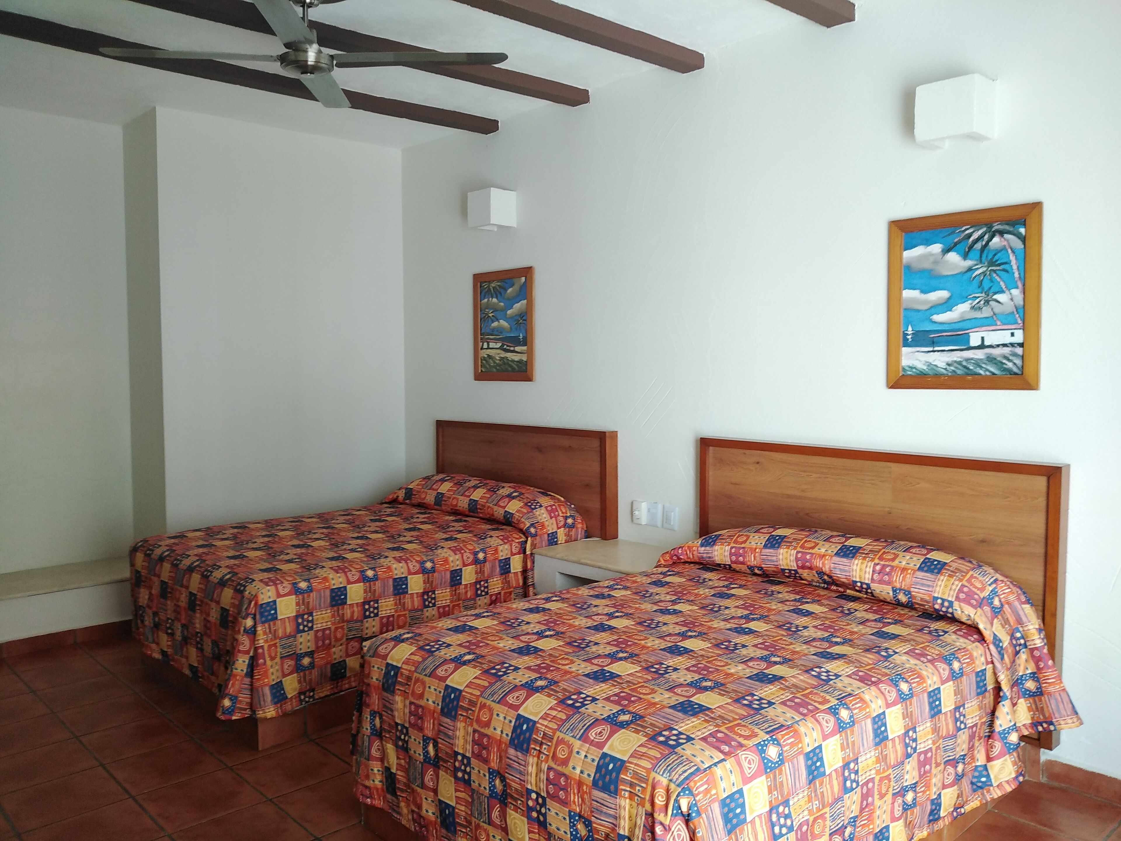 Una habitación con dos camas, un ventilador de techo y dos lámparas fijadas a la pared.