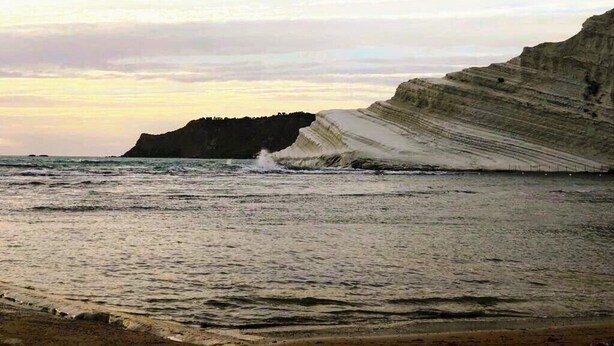 A coastal landscape with layered cliffs and a beach.