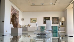 A spacious living room with a glass coffee table, modern furniture, and artwork on the walls.