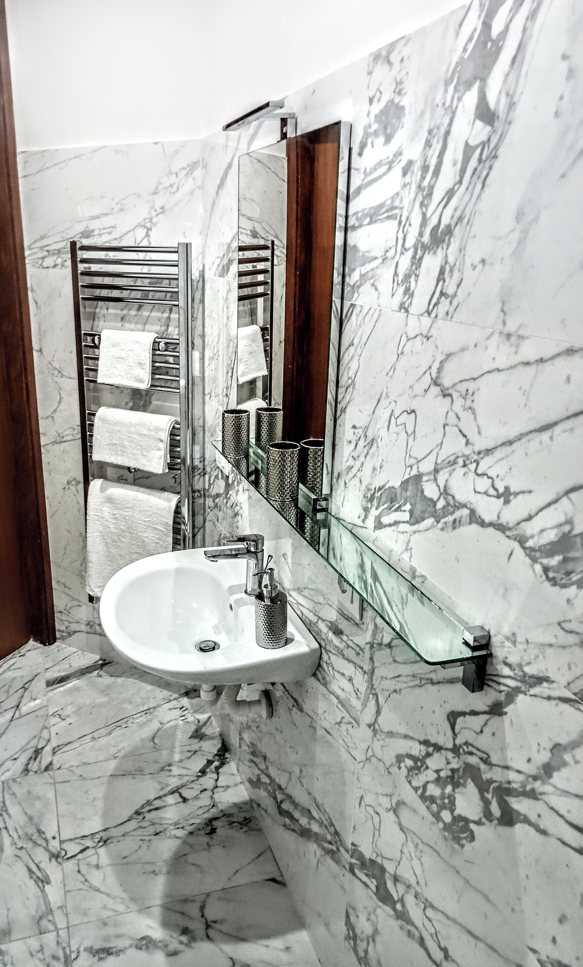 A bathroom with a marble sink, a glass shower enclosure, and a mirror reflecting a towel rack and a towel.