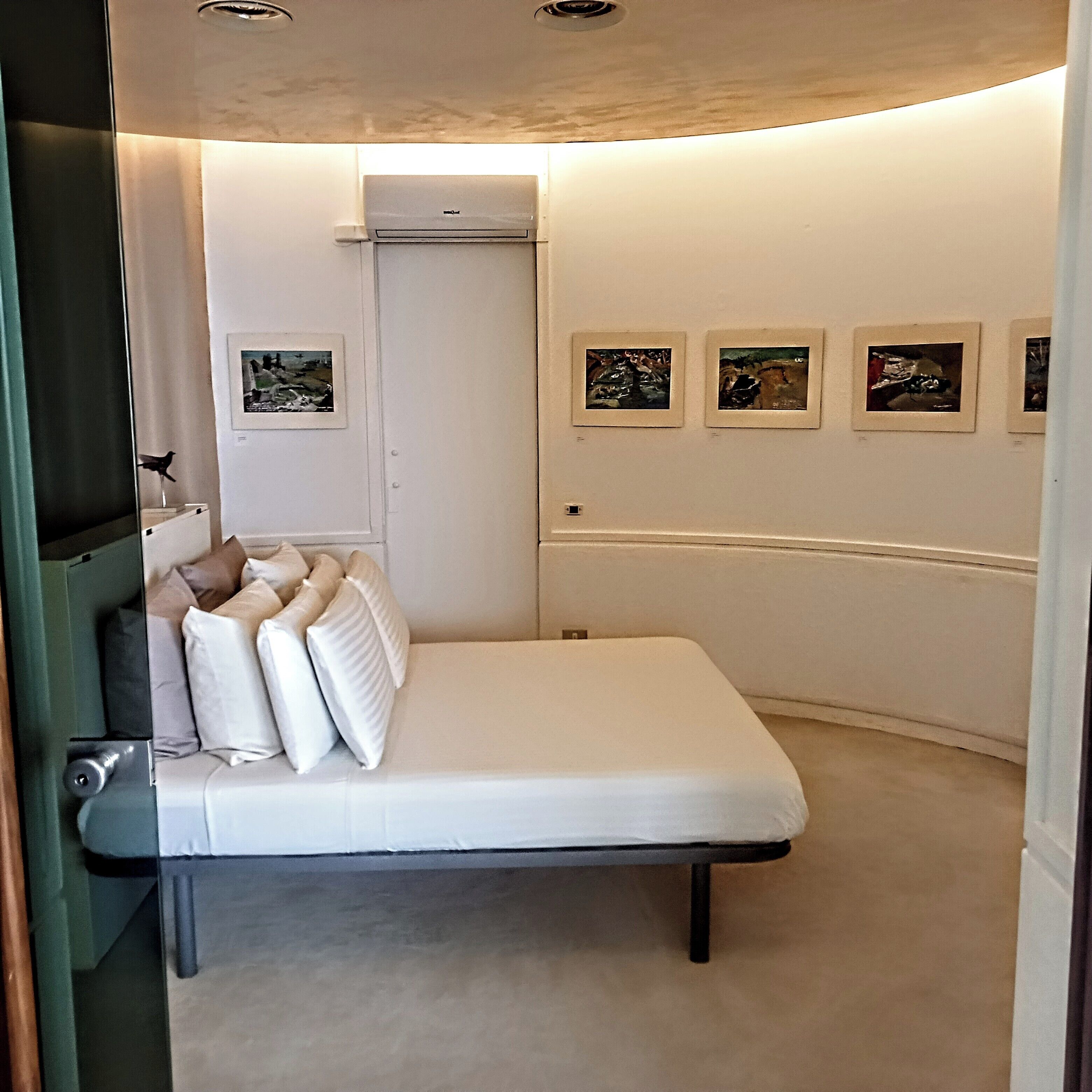 A bedroom with a bed, a door, and four framed pictures on the wall.
