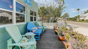 A wooden deck with outdoor seating, a church in the background, and a signboard on the building. - Naut 2 Shabby Cottage-Awesome Pool Area, Pine Ave location close to everything (Anna Maria)