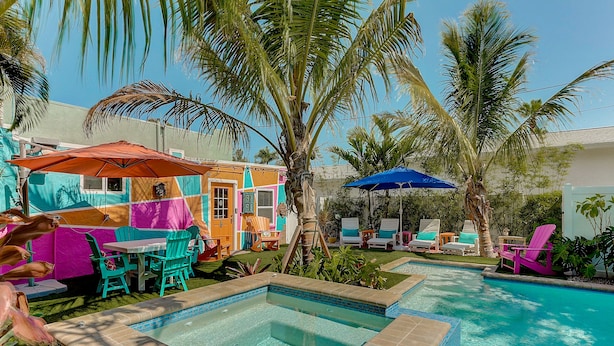 A swimming pool with a tiled edge, surrounded by palm trees and colorful outdoor furniture. - Naut 2 Shabby Cottage-Awesome Pool Area, Pine Ave location close to everything (Anna Maria)
