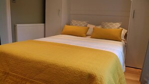 A bed with a yellow quilt and patterned pillows, a radiator, and a wardrobe. - 2-Bed, Sleeps 4, Garden (London)