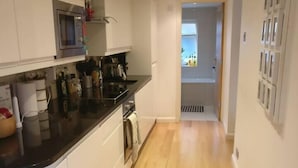 A modern kitchen with white cabinets, a black countertop, and a microwave. - 2-Bed, Sleeps 4, Garden (London)