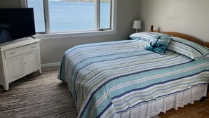 A bedroom with a bed, a television on a dresser, a window with a view of the sea, and a lamp on the nightstand. - Spectacular views, close to down town Rockland (Owls Head)