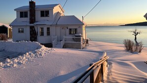 A two-story house with a snow-covered porch and a view of a calm lake. - Spectacular views, close to down town Rockland (Owls Head)