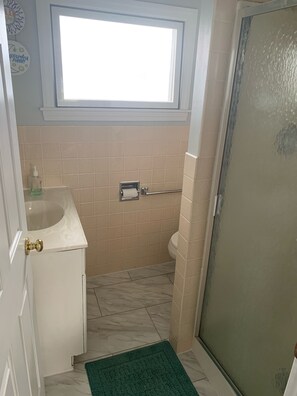 Et badeværelse med vindue, toilet, vask og bruseområde.