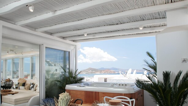 Un espace repas moderne avec une table en bois, des chaises blanches et une vue sur la mer.