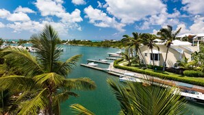 Uma marina com barcos atracados, um edifício branco com piscina e palmeiras.