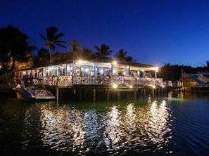 A waterfront building with a glass facade, a deck, and a boat docked nearby.